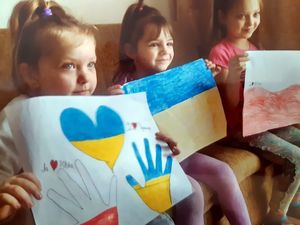 Troje dzieci siedzi na kanapie w pomieszczeniu, dzieci trzymają w rękach rysunki