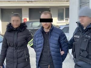 Dwoje policjantów prowadzi zatrzymanego mężczyznę, który ma założone kajdanki