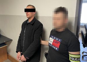 Zatrzymany mężczyzna z założonymi kajdankami, obok policjant ubrany po cywilnemu