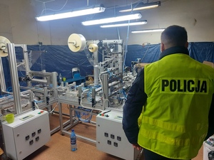 nieumundurowany policjant w kamizelce z napisem Policja stoi przy maszynie do produkcji nielegalnych papierosów