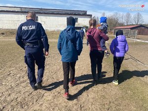 dzielnicowy oraz matka z 3 dzieci idą po terenie stadniny - fotografujący stoi za nimi