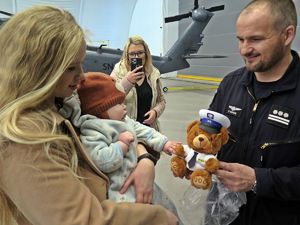 kobieta trzyma dziecko na ręku a policjant wręcza im misia - policyjną maskotkę