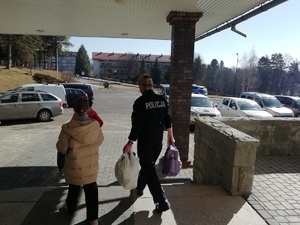 umundurowana policjantka niesie bagaże kobiety, która idzie obok  z dzieckiem na ręku - widok z tyłu