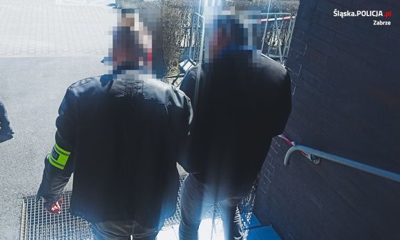 policjant prowadzi zatrzymanego - widok z tyłu