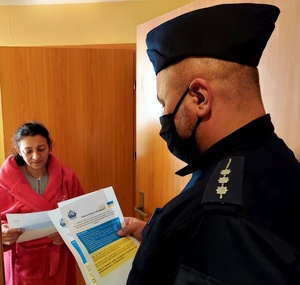 umundurowany policjant rozdaje ulotki informacyjne uchodźcom