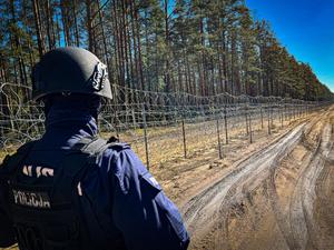 policjant stoi przy płocie na granicy