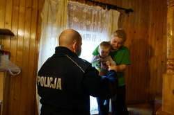 Na zdjęciu mundurowy w jednym z domów na terenie miasta, w którym przebywają uchodźcy. Policjanci wręcza dziecku  gadgety z kampanii &quot;Mamo, Tato tutaj jestem&quot; w postaci czapki i opaski silikonowej