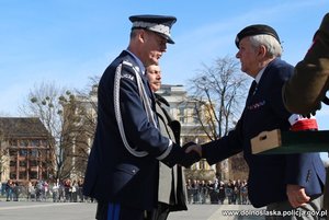 komendant wojewódzki Policji we Wrocławiu stoi na placu z mężczyzną ubranym w stój wojskowy z czasów II wojny światowej oraz gratulujący mu mężczyzna