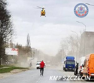 śmigłowiec LPR lądujący na ulicy, na której stoi mężczyzna, na poboczu stoją samochody