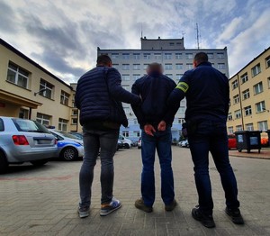 dwaj policjanci prowadzą zatrzymanego - widok z tyłu