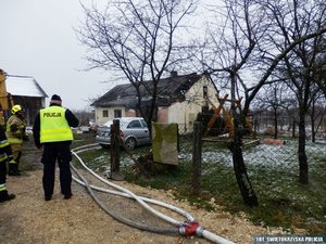 na pierwszym planie umundurowany policjant ze strażakami, w tle budynek