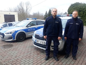 dwaj policjanci stoją przed radiowozem