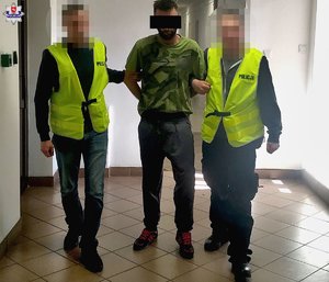 dwóch policjantów trzyma zatrzymanego mężczyznę w kajdankach