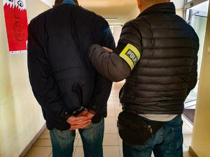 policjant z zatrzymanym mężczyzną w kajdankach