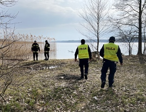 policjanci wspólnie ze strażakami szukają zaginionej na terenie leśnym, przy brzegu zbiornika wodnego