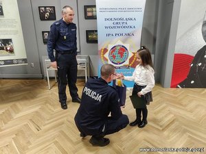 policjant wręcza dziewczynce nagrodę, drugi policjant stoi