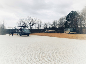 Płyta lądowiska śmigłowców, a na niej zaparkowany Black Hawk. W oddali śmigłowiec Mi-2, nieopodal autobus.