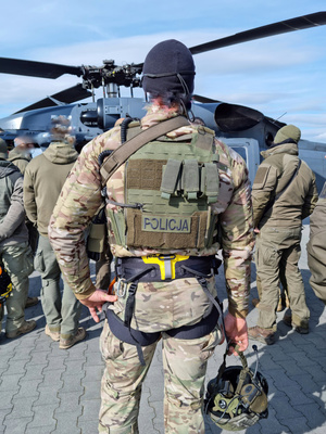 Na tle stojącego bokiem Black Hawka policjanci sfotografowani od tyłu.