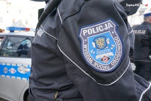 widoczna naszywka z napisem policja Cieszyn Wydział Ruchu Drogowego na mundurze policjanta stojącego przy radiowozie