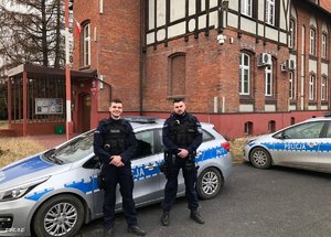 dwaj umundurowani policjanci przed radiowozem