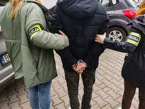policjanci stoją z zatrzymanym mężczyzną w kajdankach
