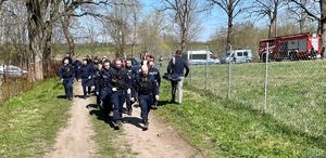 grupa policjantów biorąca udział w poszukiwaniach zaginionego dziecka, z tyłu widoczne są radiowozy i strażak na quadzie
