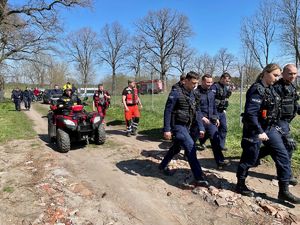 grupa policjantów biorąca udział w poszukiwaniach zaginionego dziecka, z tyłu widoczne są radiowozy i strażak na quadzie