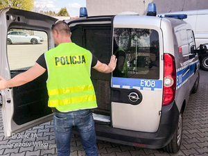 Policjant w żółtej kamizelce z napisem Policja zamyka drzwi radiowozu