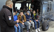 Dzieci siedzą na pokładzie helikoptera, obok stoi pilot i opowiada o maszynie.
