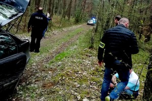 &quot;las, policjanci pilnują zatrzymanego mężczyzny, w tle widać radiowozy policjyjne