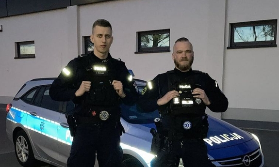 dwaj policjanci stoją przed radiowozem