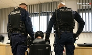 Policjanci stoją przy zatrzymanym mężczyźnie, który siedzi na krześle