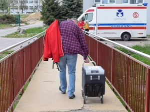 mężczyzna ciągnie specjalny pojemnik na kółkach, w którym znajduje się serce do przeszczepu, w tle ambulans