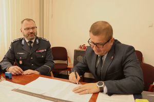 umundurowany policjant siedzi za stołem wraz z mężczyzną w garniturze, który podpisuje dokument