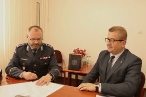 za stołem siedzi mężczyzna w garniturze i umundurowany policjant, który podpisuje dokument