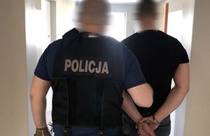 policjant prowadzi zatrzymanego, który ma ręce skute w kajdanki