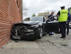 czarny samochód marki bmw po zderzeniu ze ścianą budynku, obok stoi policjant ustalając czynności zdarzenia