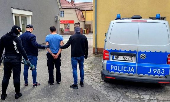 trzej policjanci z zatrzymanym mężczyzną, obok stoi radiowóz