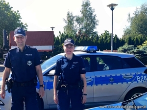 policjant i policjantka stoją przy radiowozie