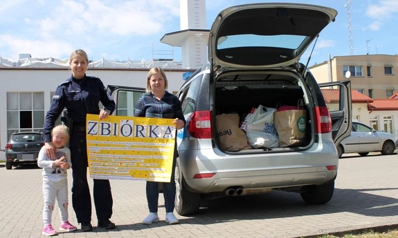 policjantka z kobietą przy samochodzie trzymają karton z napisem zbiórka, obok policjantki dziecko