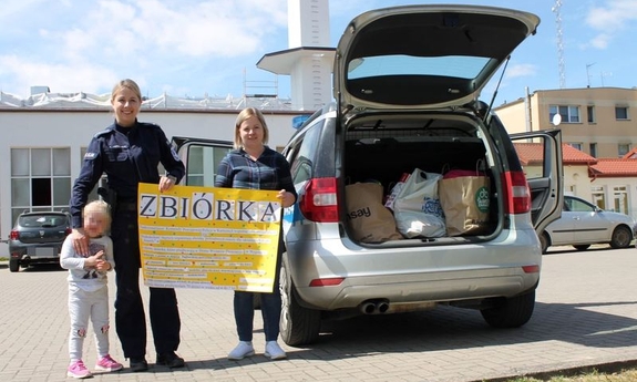 policjantka z kobietą przy samochodzie trzymają karton z napisem zbiórka, obok policjantki dziecko