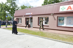 uczestnicy uroczystości, ksiądz idzie wzdłuż budynku