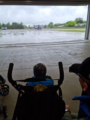 Przez otwarte wrota hangaru policyjnych śmigłowców dziecko siedzące w wózku patrzy na stojący w oddali śmigłowiec Black Hawk.