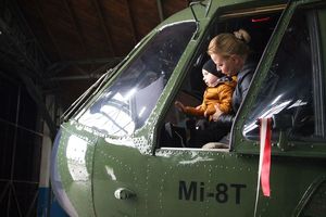 Zdjęcie wykonane z boku dziobu policyjnego śmigłowca Mi-8. W otwartym oknie maszyny siedzi na miejscu pilota kobieta, a na jej kolanach kilkuletni chłopiec w żółtej kurtce.