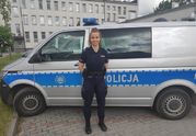 policjantka pozuje do zdjęcia, za nią stoi radiowóz