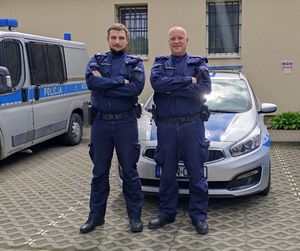 dwaj policjanci stoją przed radiowozem