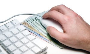 klawiatura komputera i dłoń oparta na myszce pod którą znajduje się gotówka
