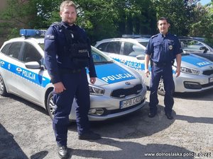 dwaj policjanci stoją przy radiowozie