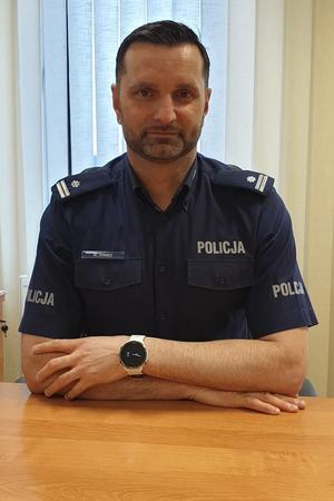 siedzący za stołem policjant pozuje do zdjęcia