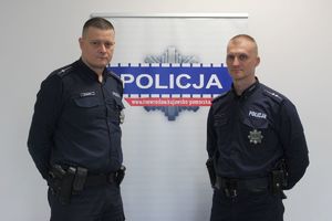 dwaj policjanci pozują do zdjęcia, między nimi widoczny jest napis Policja na ścianie